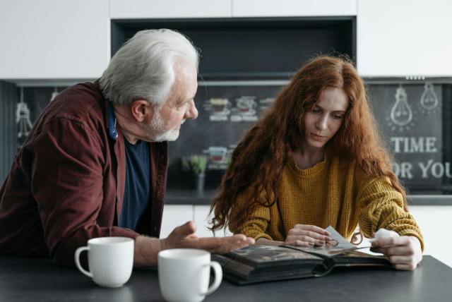 Elderly man and young woman looking at a photo album together, evoking emotions and memories.