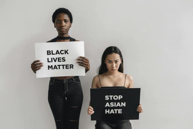 Two women holding protest signs for Black Lives Matter and Stop Asian Hate against a plain background.