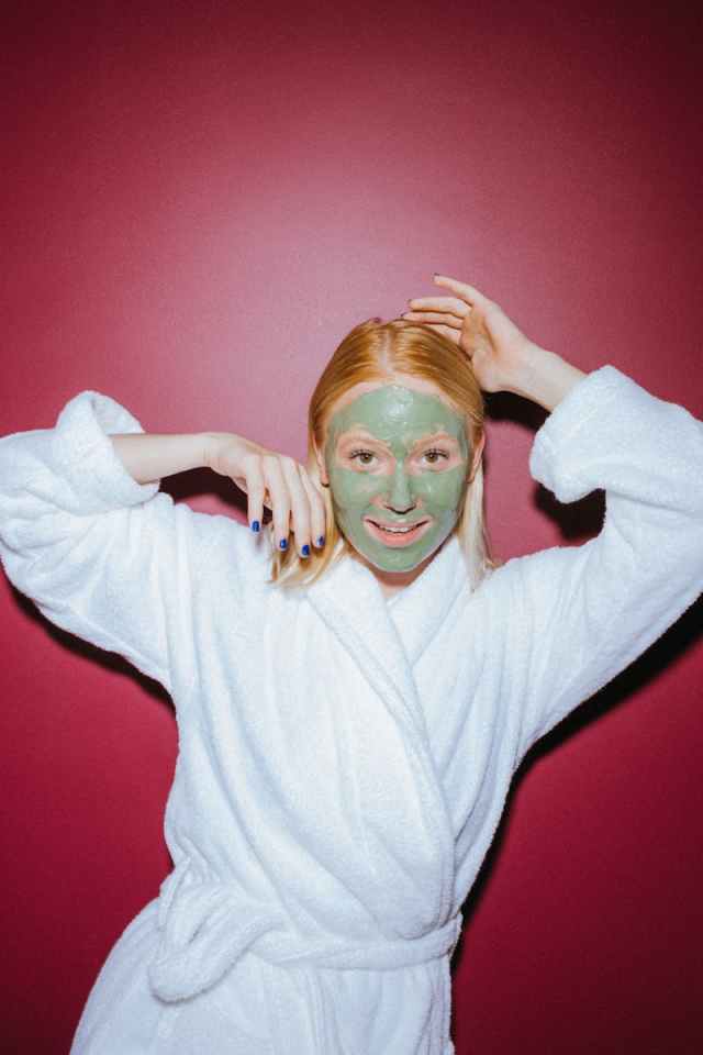Woman enjoys skincare routine with a green facial mask, enhancing her beauty and relaxation.