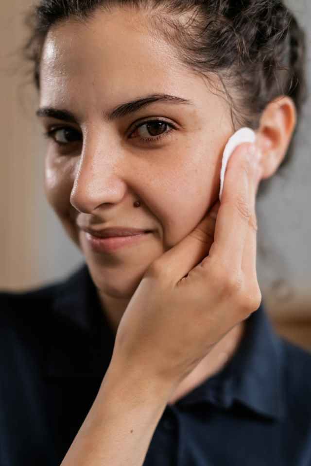 Close-up of a woman smiling while cleansing her face with a cotton pad.