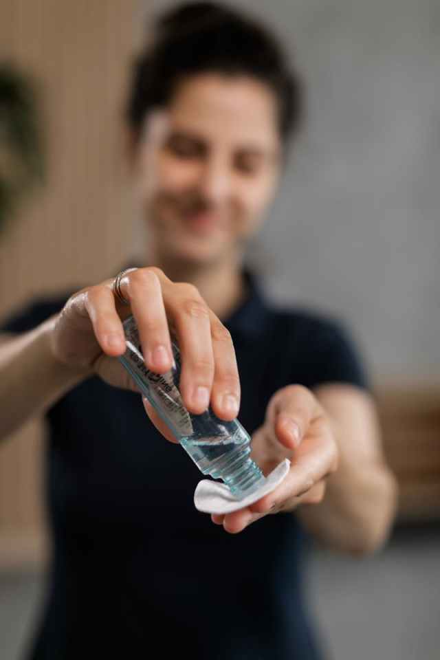Blurred woman using skincare toner on cotton pad in bathroom setting.