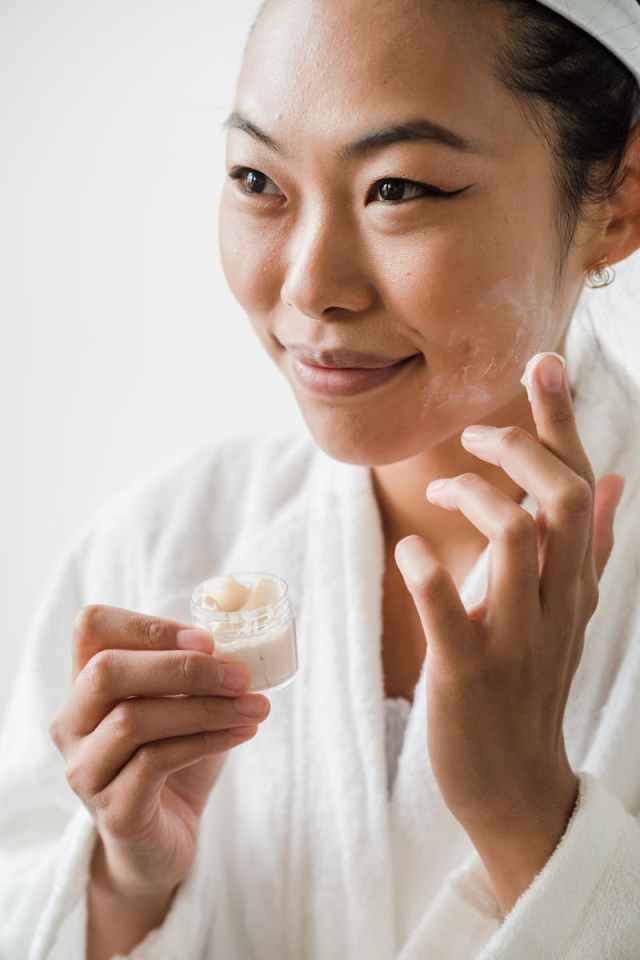 Close-up of an Asian woman applying moisturizer during her skincare routine.