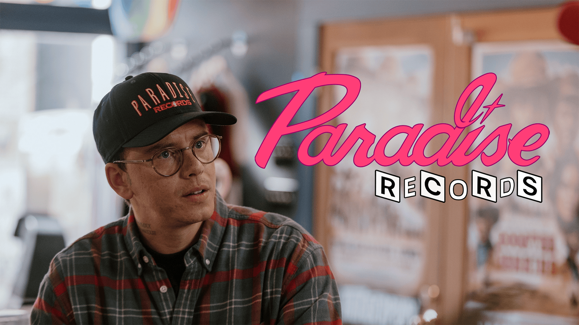 Promotional still from Paradise Records, showing a record store setting with the Paradise Records logo and a Logic wearing a Paradise Records cap