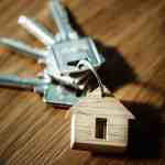 selective focus photography of four silver keys with brown house keychain on brown surface