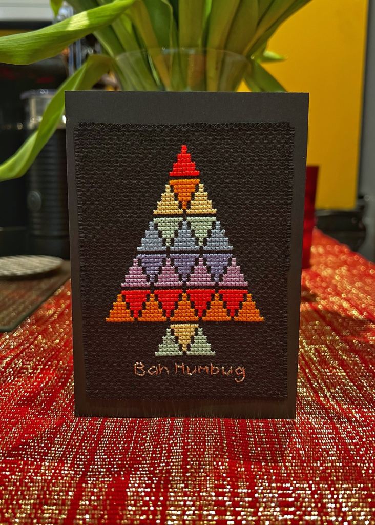 Completed cross-stitch of a Christmas tree made of colourful roes of triangles and the saying "Bah Humbug" underneath