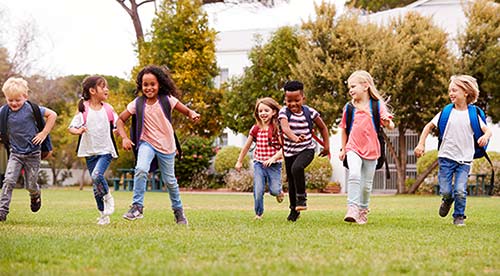 Happy group of elementary school students running across a field