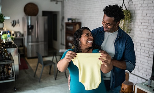 Happy couple in their kitchen, admiring a baby onesie