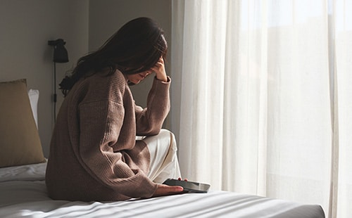Sad woman sits on her bed after reading bad news on phone