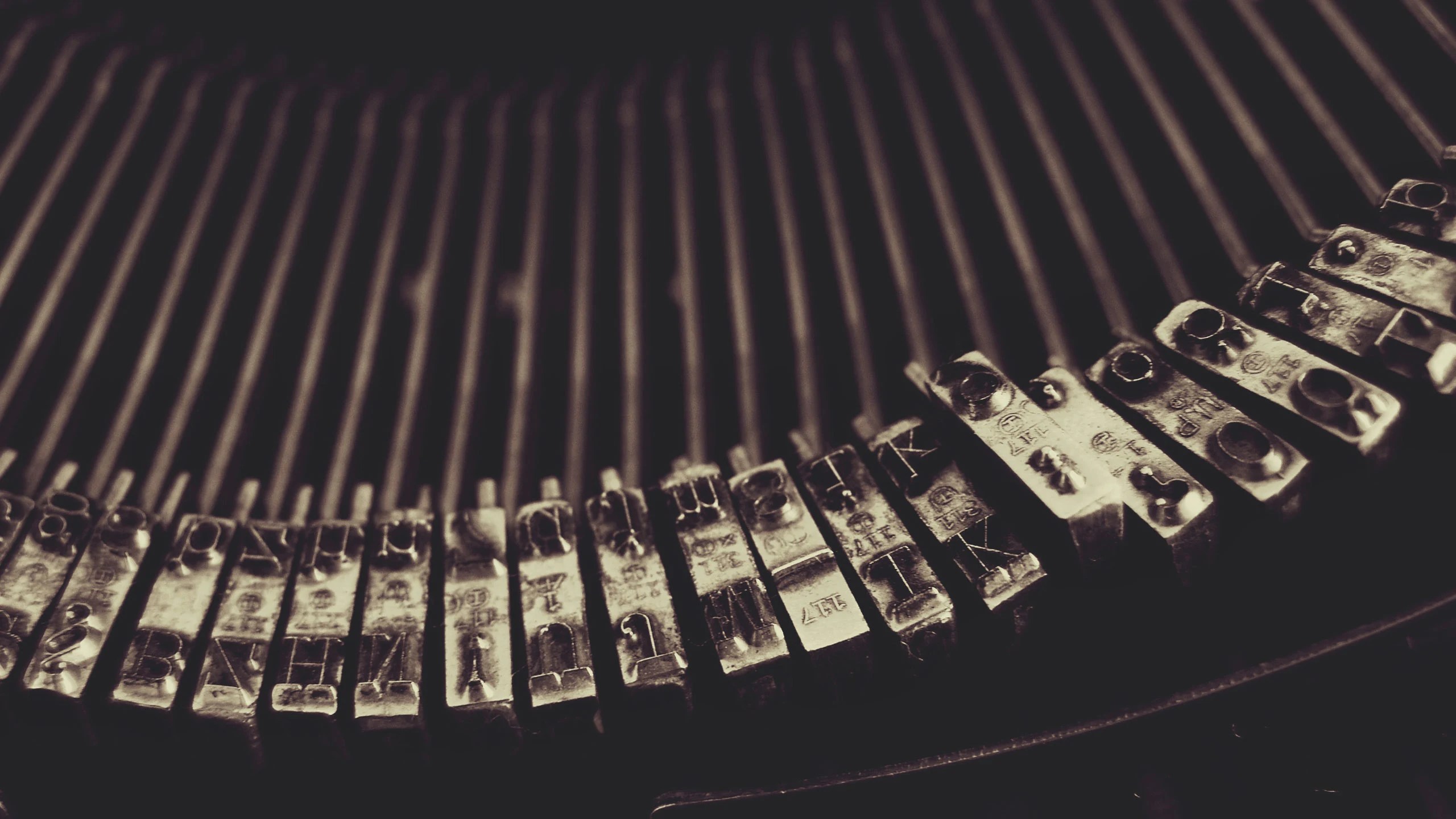 Close-up view of metal typebars inside a vintage typewriter, with the letters and symbols clearly visible on each bar, and the typewriter’s round, vertical metal rods blurred in the background.