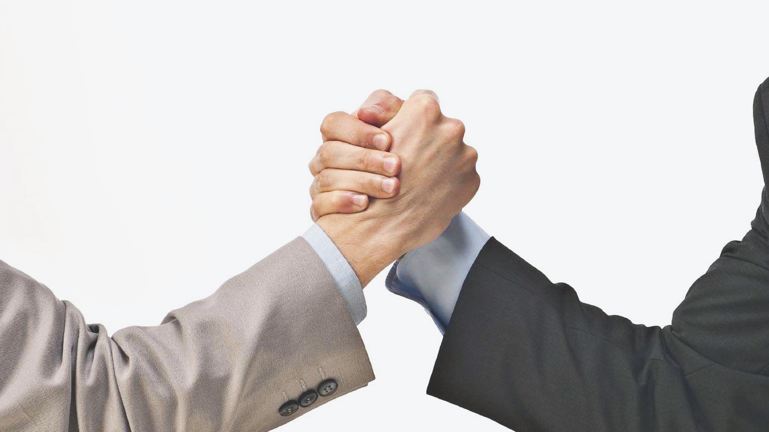 Two people are shaking hands, but their fingers are interlocked in a way that resembles an arm-wrestling grip rather than a traditional handshake. One person is wearing a light-colored suit, and the other is in a dark-colored suit, both against a plain white background.
