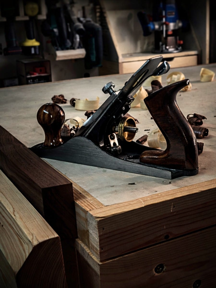 Vintage hand plane with wood shavings on workbench surrounded by woodworking tools at Lightwaves Sense handmade workshop