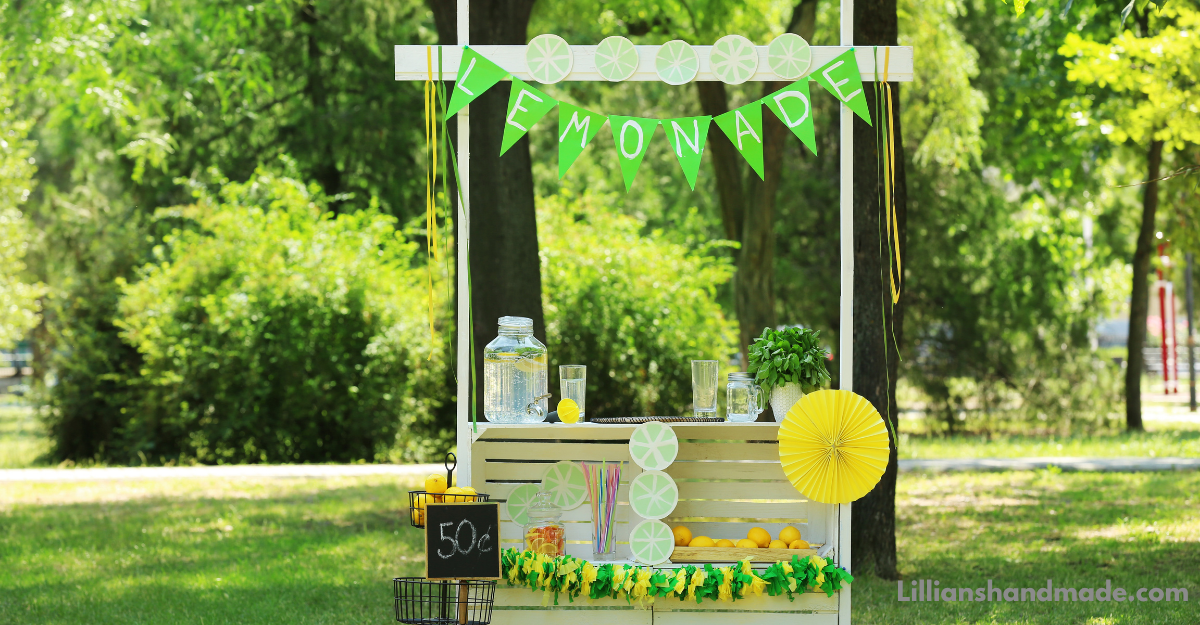 Decorated lemonade stand with lemons, glasses, and a lemonade banner in a park for a summer learning activity.
