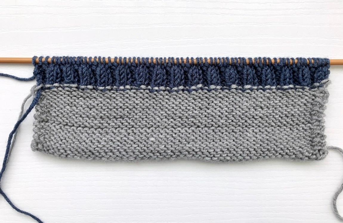 A section of knitted scarf on a bamboo knitting needle