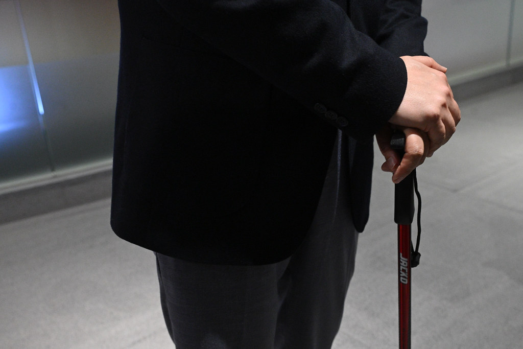 許正宇左手拄著拐杖並穿著運動鞋，在立法會緩步前行。