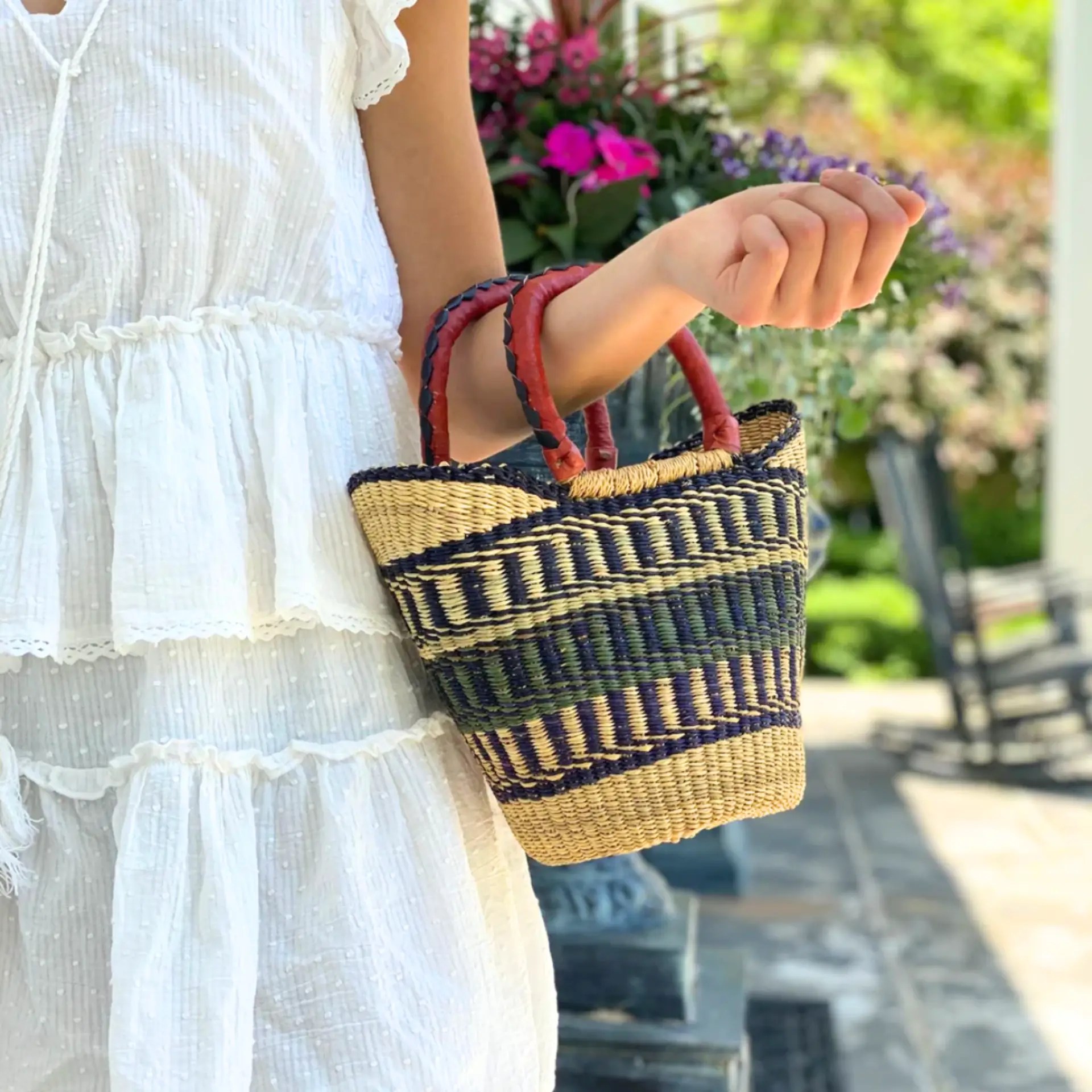 Hand-woven Bolga tote with neutral colors and leather handle, carried by a woman in a white dress.