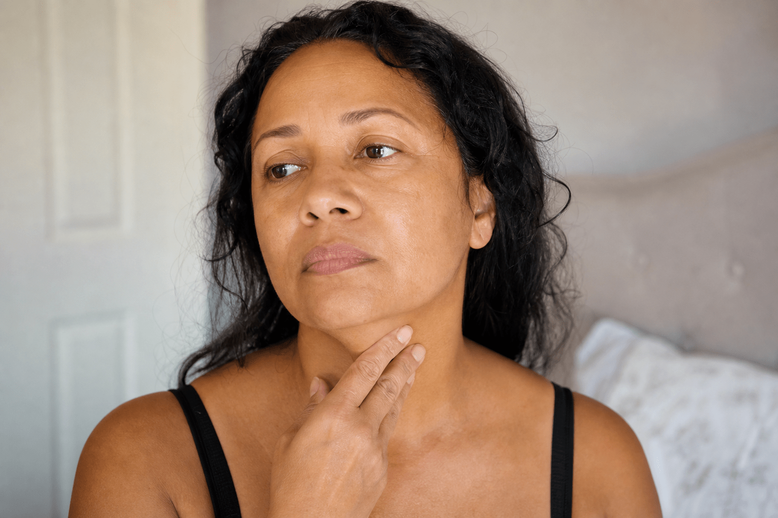 Woman gently touching her neck and throat, looking thoughtful, soft lighting