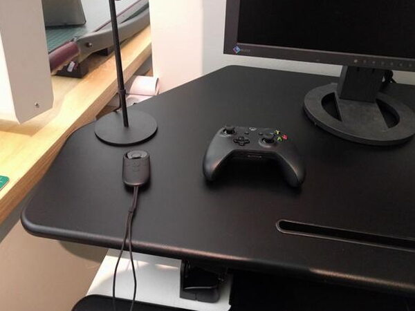 A monitor, desk lamp, and game controller arranged on the FlexiSpot desk at seated height