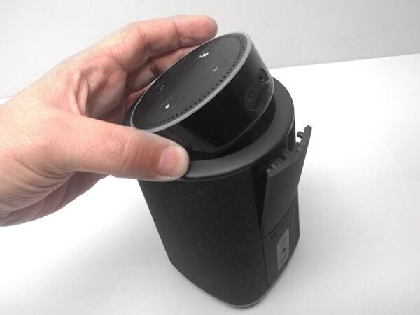 A hand lowering an Echo Dot down into the top of the Vaux speaker