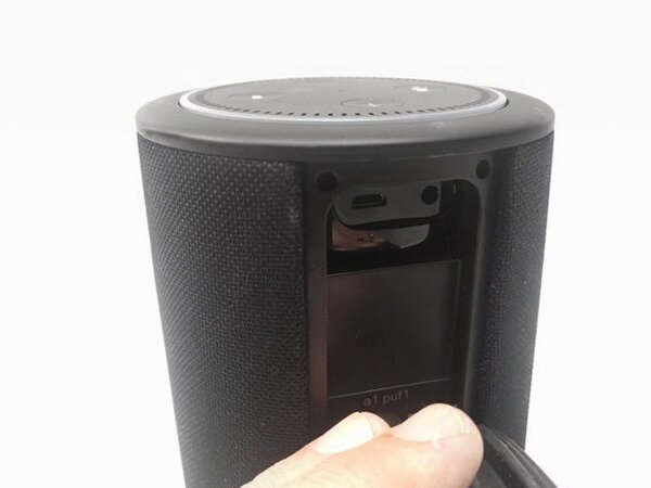 The Echo Dot seated in the Vaux with its light ring lit, a finger pressing the power button on the front panel