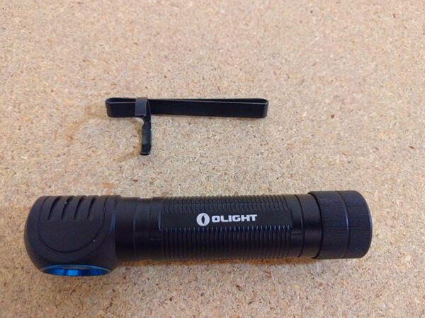 The Olight H2R Nova lying next to its removed pocket clip