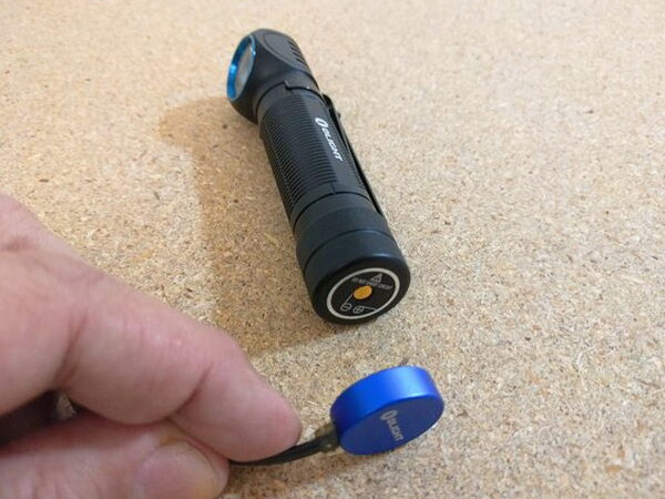 A hand peeling the magnetic charging cap off the Olight H2R Nova tailcap