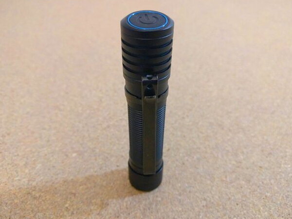 The Olight H2R Nova standing on its tail with the top power button visible