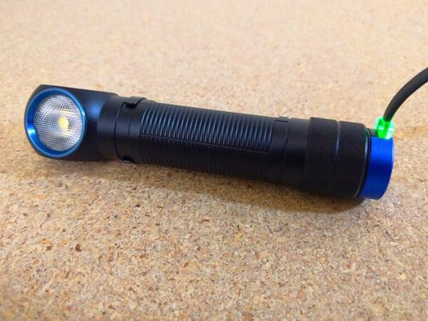 The Olight H2R Nova charging at an angle with a green LED signaling a full battery