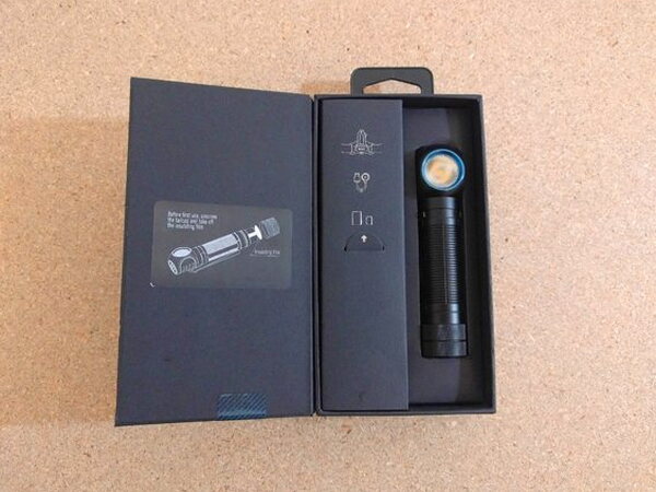 The Olight H2R Nova nested inside its open box next to a printed first-use reminder