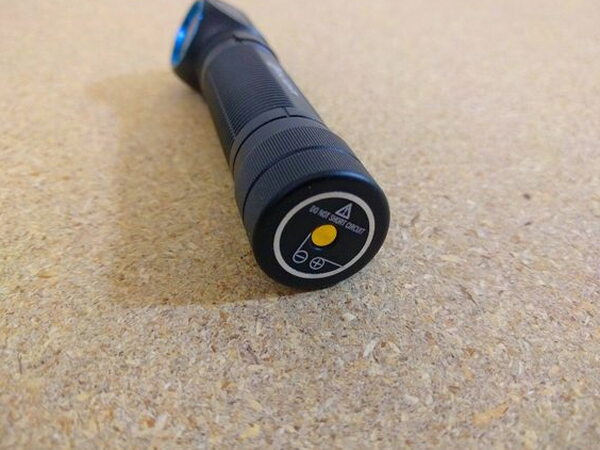A close-up of the Olight H2R Nova tailcap with polarity markings and a short-circuit warning