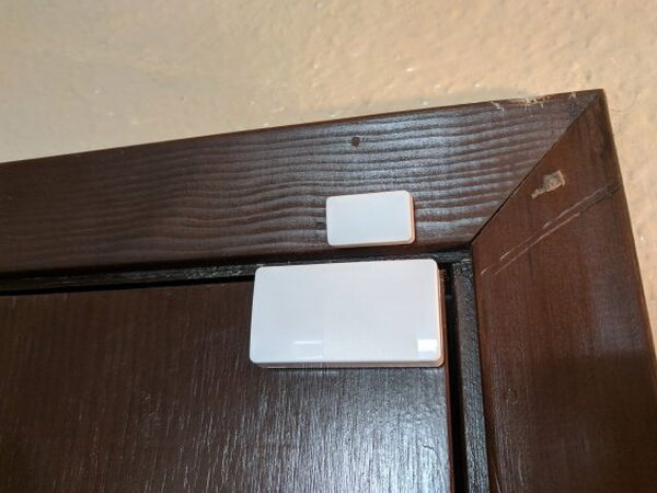 Abode Mini Door Sensor mounted on dark wood trim above a doorway