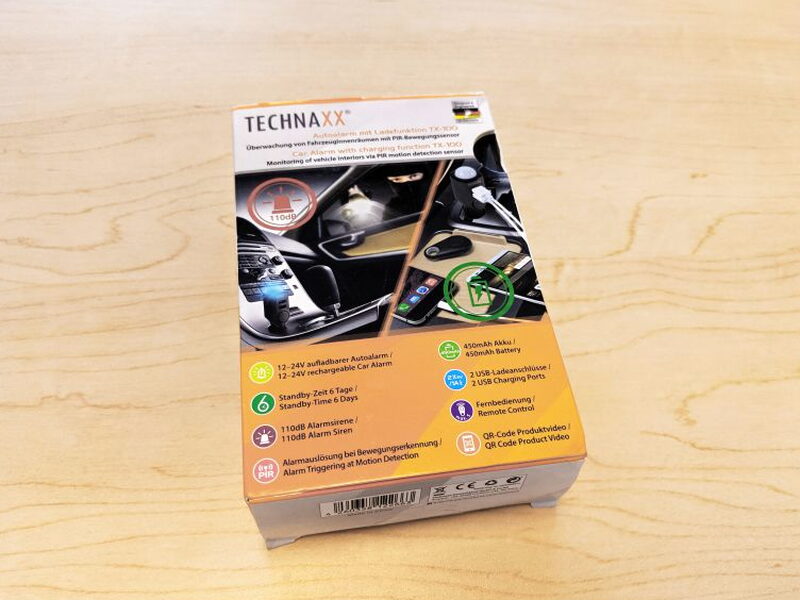 The front of the Technaxx TX-100 retail box lists the alarm, standby, USB, remote, and battery features.