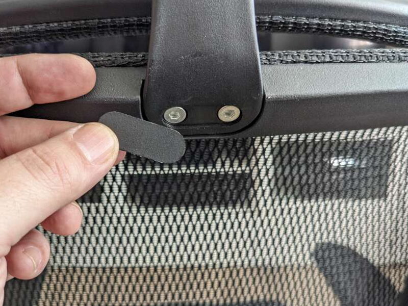 Fingers holding the plastic cover next to the headrest’s exposed mounting screws.