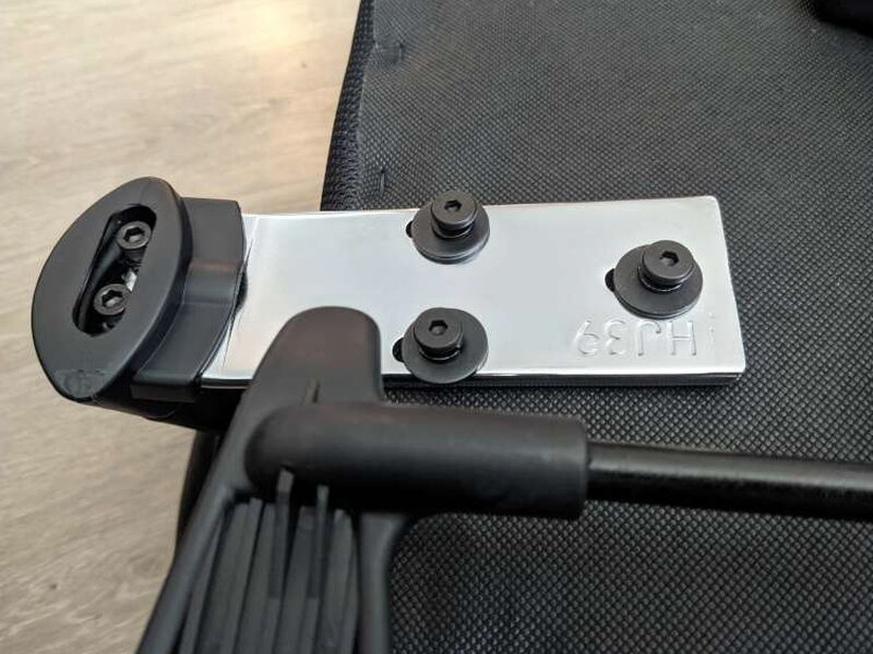 An armrest’s mounting plate and bolts, Allen wrench resting alongside on the seat’s underside.