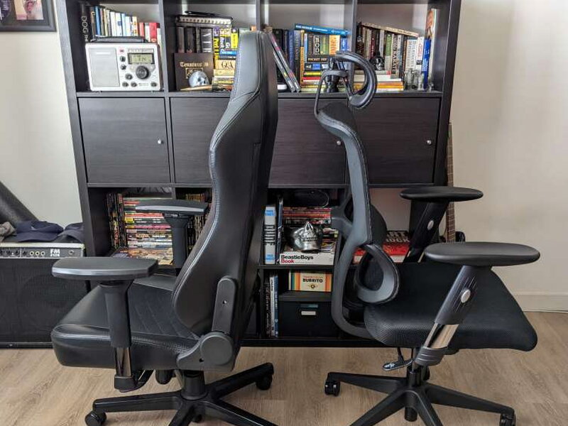 Both chairs from behind, the Hero’s padded bulk next to the M4’s thin mesh frame.