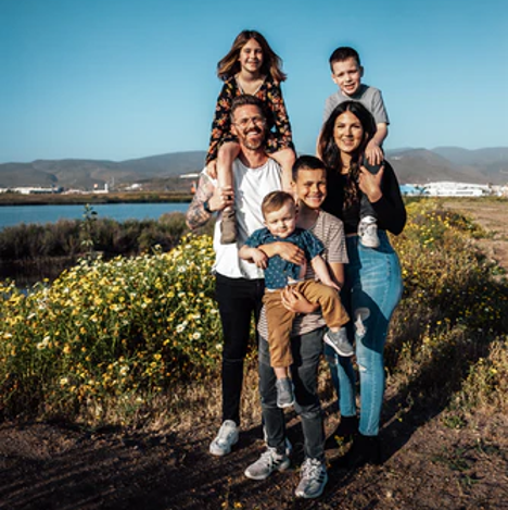 Une famille de 6 personnes eureuse en vacances devant un paysage de dunes en fleurs avec la mer