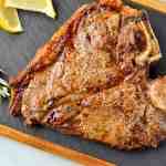 An air fryer cooked porterhouse steak on a cutting slate before being sliced.