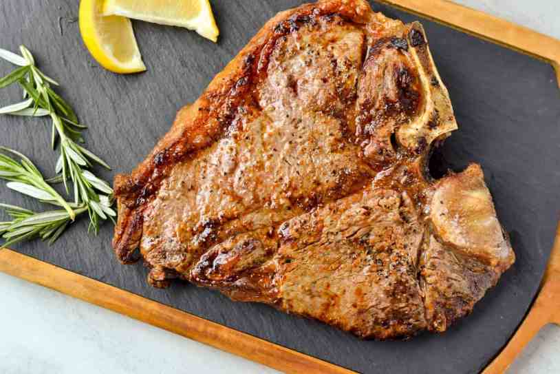 An air fryer cooked porterhouse steak on a cutting slate before being sliced.