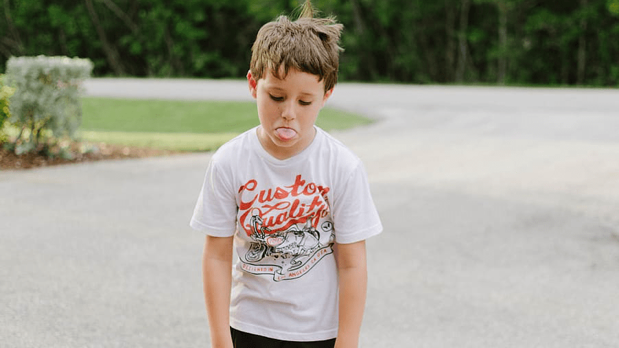A student looks down and sticks his tounge out. The image is here to depict a student with behavioral issues.
