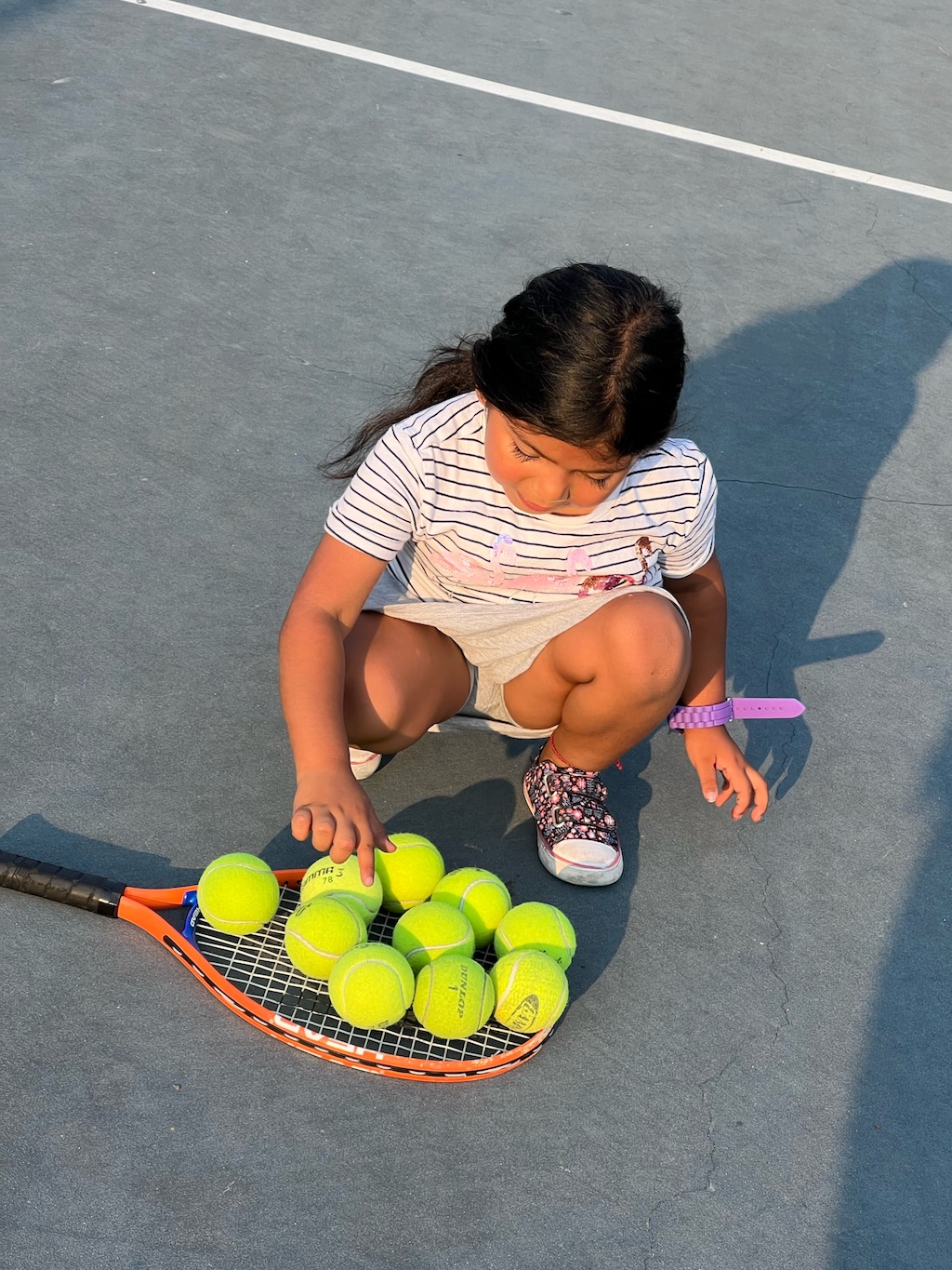 Girl on ground collecting tennis balls on her racket