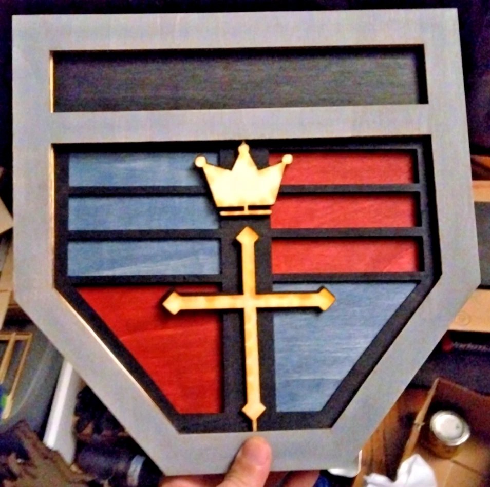 A wooden representation of the Voltron or GoLion Crest with a layered design, featuring colors blue, red, and black, along with a gold crown and black cross.