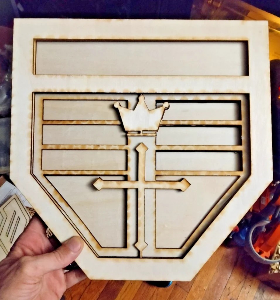 Laser-cut wooden art piece featuring the Voltron crest design with a crown and cross elements.