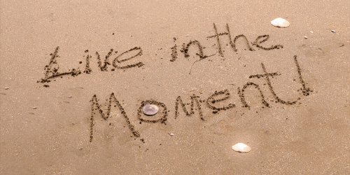 Live in the Moment text carved into wet sand