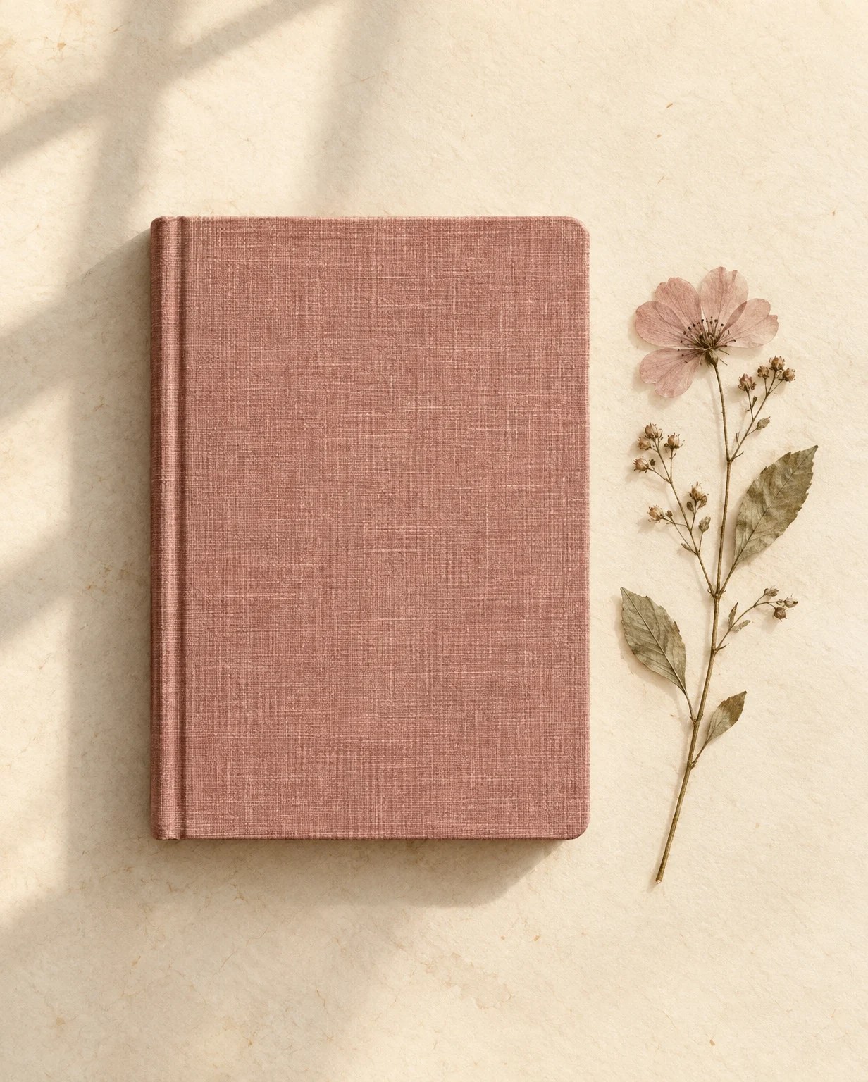 A dusty-rose notebook beside a delicate pressed flower.