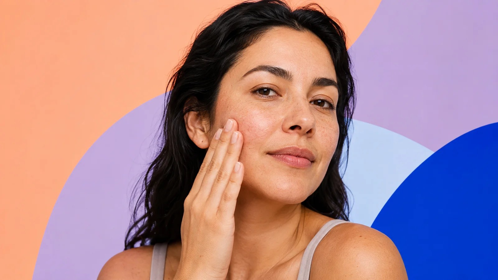 Woman gently pressing moisturizer into dry skin against a colorful geometric background