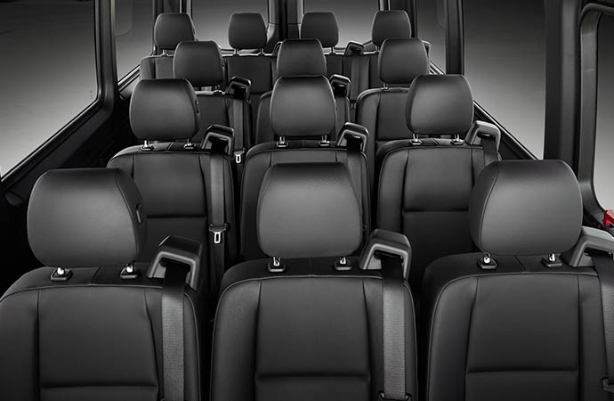 Interior view of a van or minibus showing multiple rows of black leather passenger seats with seatbelts