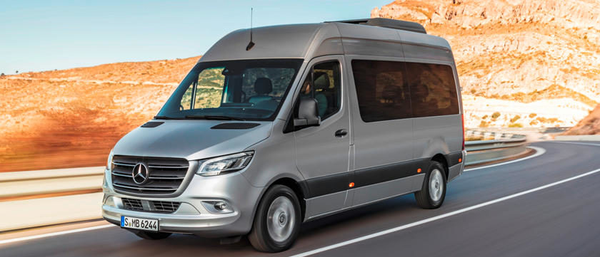 Silver Mercedes-Benz Sprinter van driving on a highway with rocky desert landscape in the background