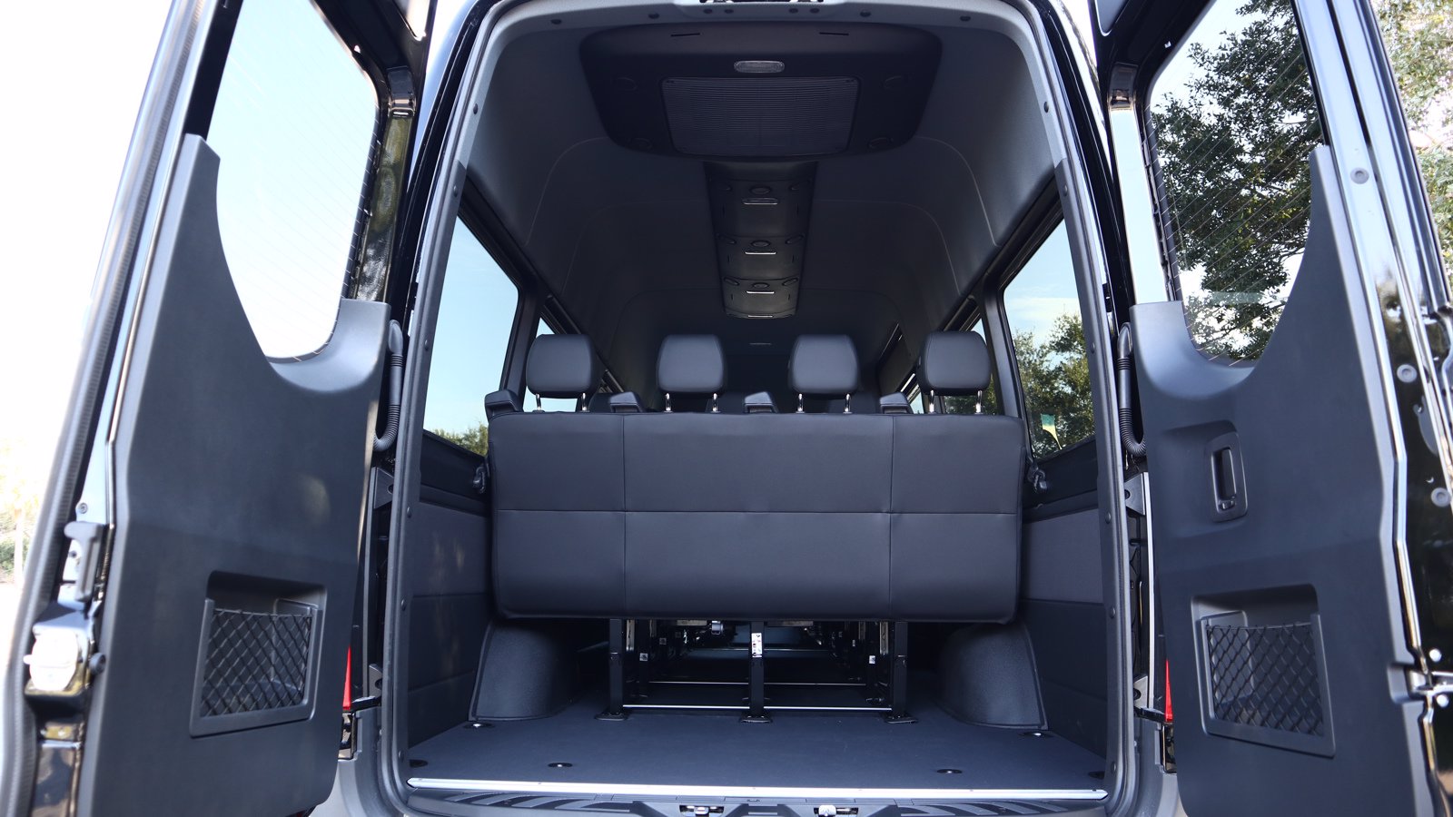 Interior of a high-roof van with open rear doors, showing rows of black leather seats and a flat cargo floor