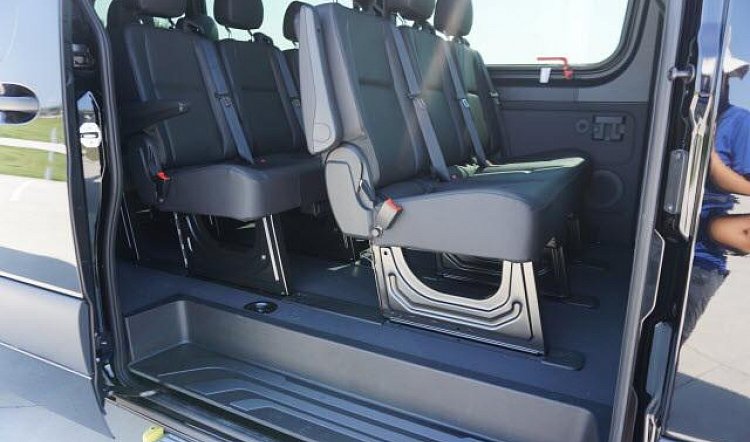 Interior of a passenger van with multiple rows of black seats, viewed through an open sliding door