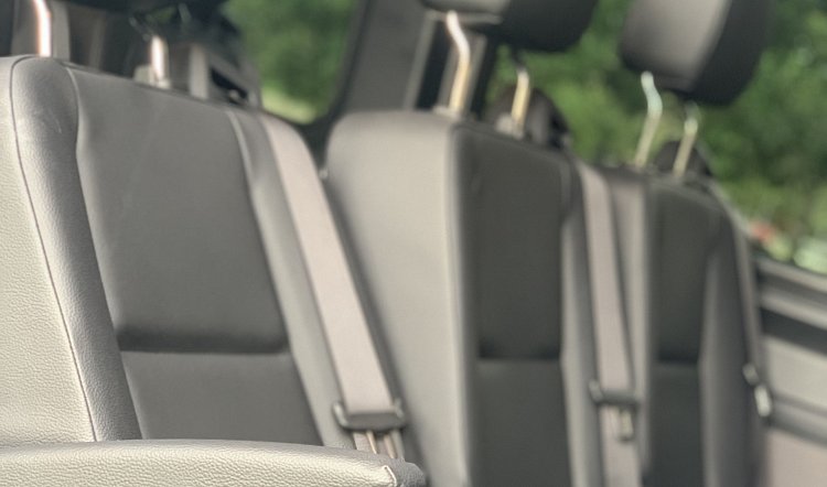 Rows of gray leather passenger seats with seatbelts inside a van or shuttle vehicle