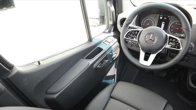 Mercedes-Benz vehicle interior showing the steering wheel with logo, dashboard, and driver's seat with black upholstery